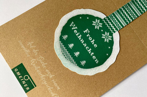 Weihnachtsmailing für Gmeiner mit grünem Ohrenschützer im Strickmuster-Design und Aufschrift ‚Frohe Weihnachten‘.
