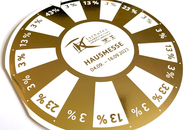 Direct-Mailing von Tschofen Raumgestaltung zur Hausmesse 2023 in Form einer goldenen Glücksscheibe mit Rabattangaben.
